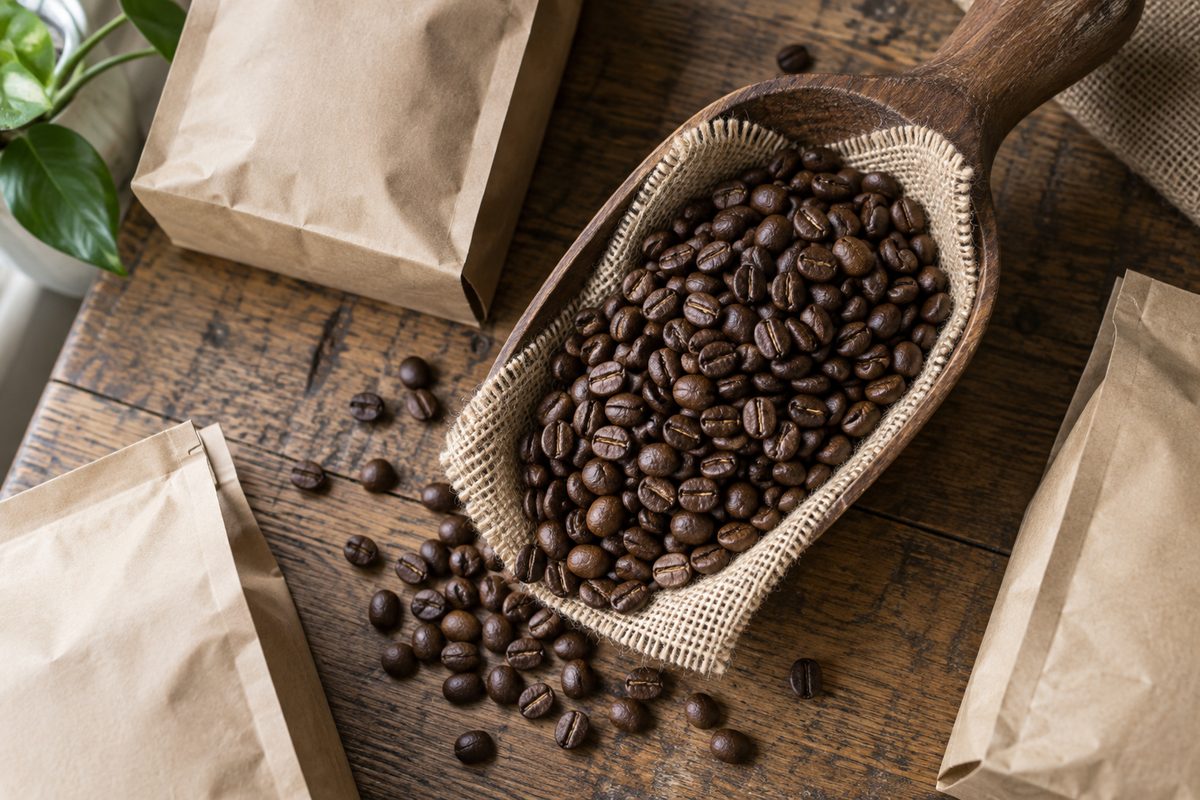Granos de café tostado en una pala de madera junto a bolsas de papel kraft